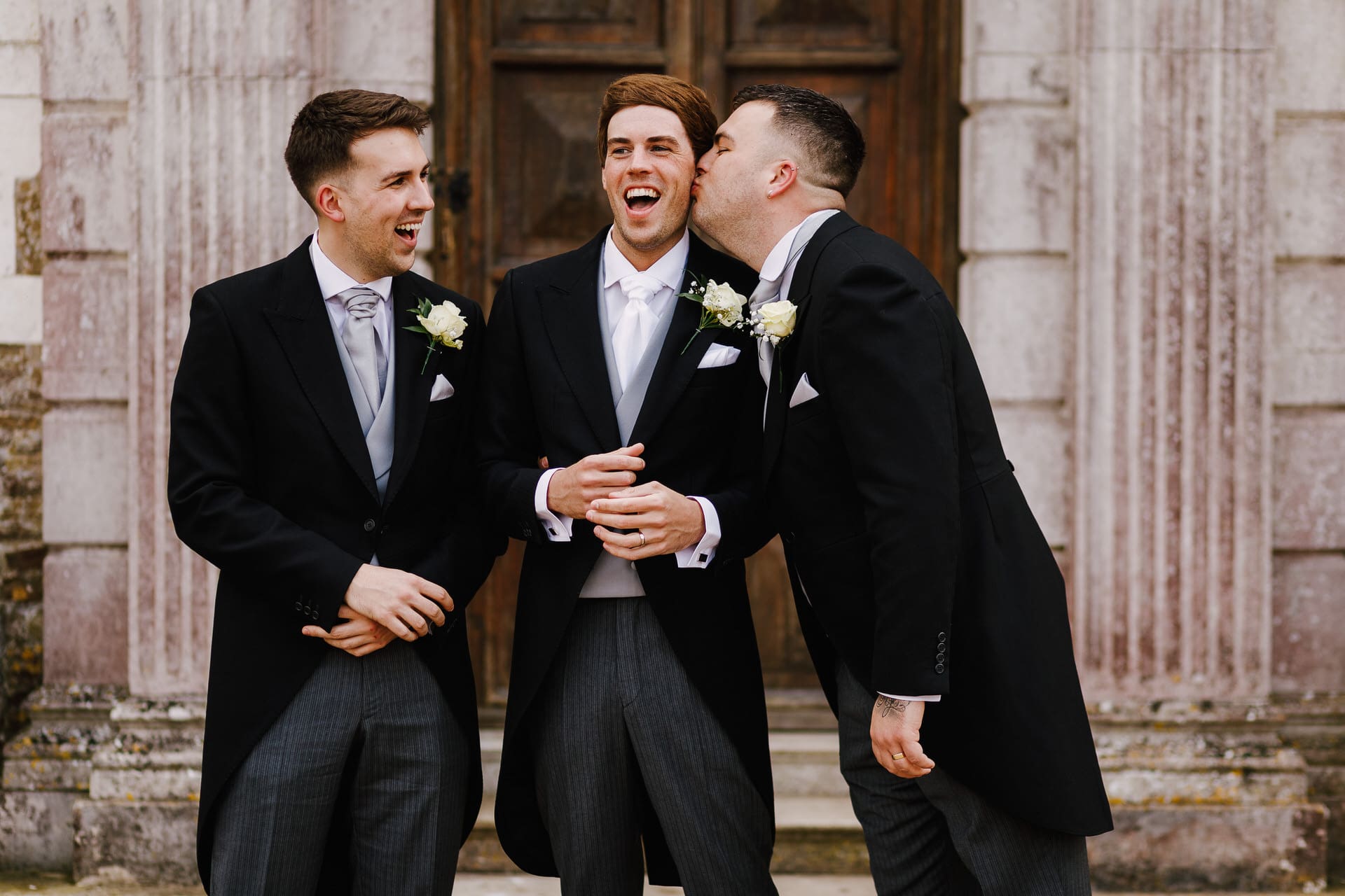 Groomsmen laughing outside main house at Loseley Park Wedding